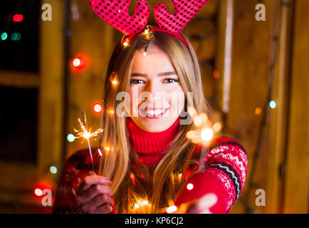 Bellissima ragazza con luci festose che indossa un maglione rosso in un log house Foto Stock