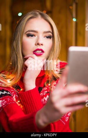 Ragazza tenendo un selfie indossando un festoso inverno rosso maglione Foto Stock