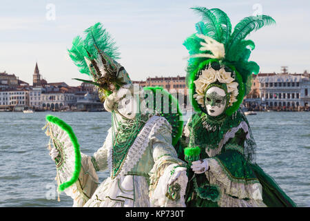 Il Carnevale di Venezia, Veneto, Italia. Due donne nel classico verde maschere e costumi che pongono insieme presso la laguna al tramonto Foto Stock