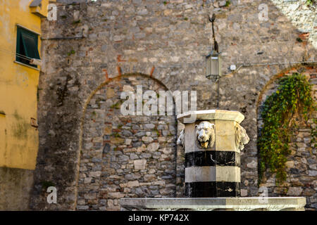 Una fontana in pietra con teste di leone nel piccolo cortile interno la sezione di parete di Portovenere Italia Foto Stock