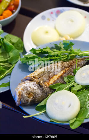 Vista dettagliata di pesce alla griglia e servita con verdure verdi e cipolla. Foto Stock