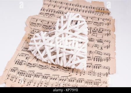 Un cuore formato con colore bianco di ramoscelli di legno su un vecchio spartito musicale Foto Stock