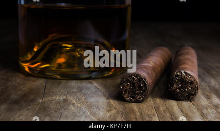 Bottiglia di whiskey con due sigari in piedi su un vecchio tavolo in legno Foto Stock