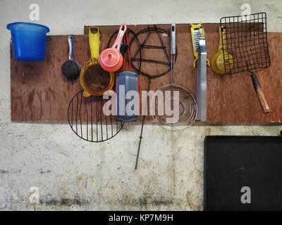 Sul bianco sporco clay appeso alla parete utensili di cucina: tazze, mestoli, mestoli, griglie per friggere, drushlat, proprio sotto il quadrato nero. Foto Stock