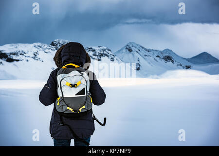 Traveler godendo di paesaggio invernale, vista posteriore della persona in piedi tra le nevi e chiedendo belle terre sulle montagne innevate, viaggio in Islanda Foto Stock