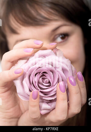 Giovane donna a pastello lilla manicure detiene un pallido fiore rosa Foto Stock