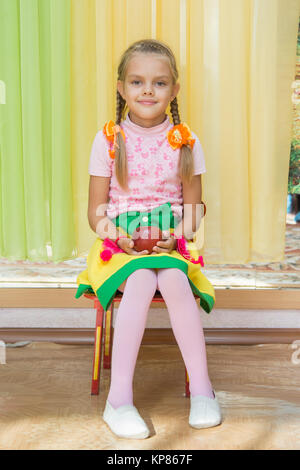 Ragazza seduta su una sedia con un Apple nella sua mano su un matinée in kindergarten Foto Stock
