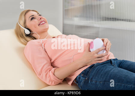 Donna incinta ascoltando Baby battito cardiaco attraverso le cuffie Foto Stock