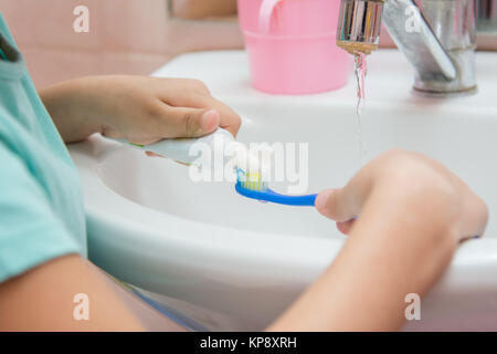 Il bambino spreme il dentifricio a partire da un tubo su uno spazzolino da denti Foto Stock