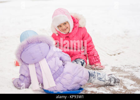 Due ragazze allegro scivolare giù per la collina di ghiaccio Foto Stock