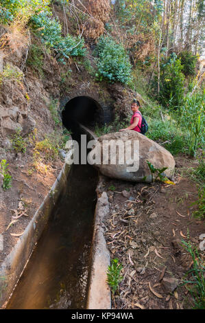 Giovane donna con proiettore prima di una caduta di massi in piedi in un levada a piedi attraverso un macinato tunnel di roccia nella parte orientale di Madera in camacha - levada dos tornos Foto Stock