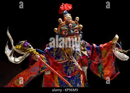 Monaco buddista esegue un ballo in maschera un antico maschera in legno di colore blu con il bianco teschi sulla parte superiore della faccia e una bandiera rossa, luminoso abiti, Foto Stock