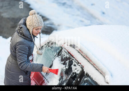 Giovane donna la sua pulizia auto da neve e gelo su una mattina di inverno Foto Stock