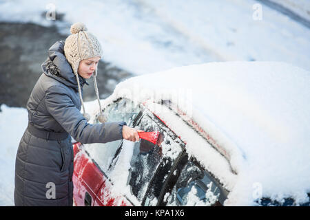 Giovane donna la sua pulizia auto da neve e gelo su una mattina di inverno Foto Stock