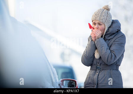 Giovane donna la sua pulizia auto da neve e gelo su una mattina di inverno Foto Stock