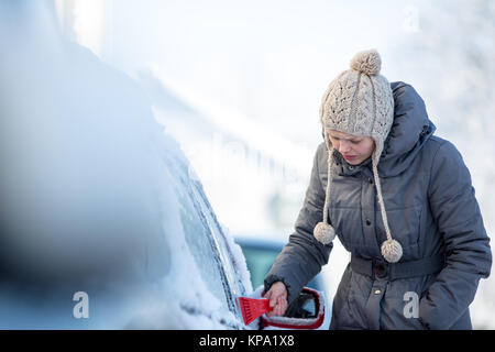 Giovane donna la sua pulizia auto da neve e gelo su una mattina di inverno Foto Stock