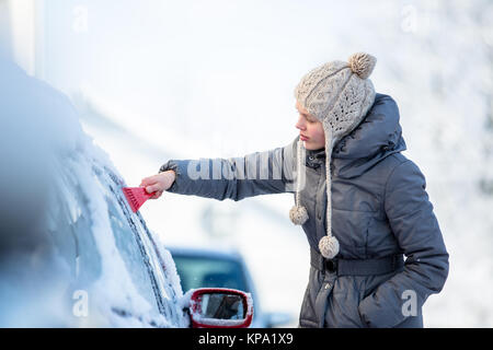 Giovane donna la sua pulizia auto da neve e gelo su una mattina di inverno Foto Stock