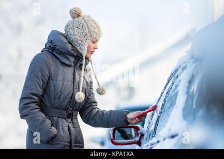 Giovane donna la sua pulizia auto da neve e gelo su una mattina di inverno Foto Stock