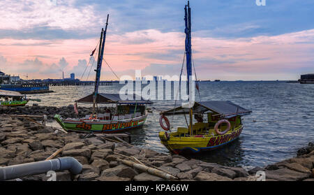 Jakarta, Indonesia - 16 Marzo 2016: barche sulla riva, tramonto colorato nello skyline di Jakarta, Java, Indonesia Foto Stock