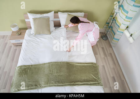 Governante femmina disponendo lenzuolo sul letto Foto Stock