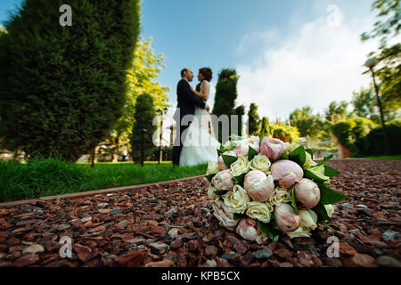 Chiudere l immagine del bellissimo bouquet nuziale giacente sul terreno con la sposa e lo sposo in sfondo sfocato Foto Stock
