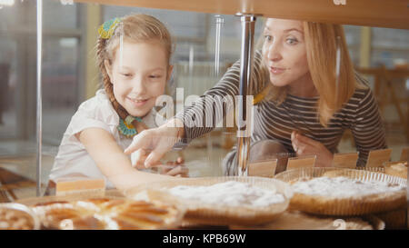 Ragazza con una spiralina e sua mamma guardare le torte nella finestra scelta Foto Stock