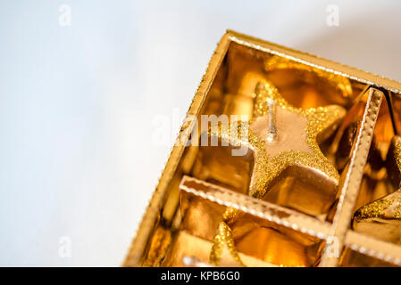 Golden scintillanti decorazioni di Natale nella casella in bianco, camera per copia. Primo piano di una festosa a forma di stella candele in gold box, camera per il testo. Foto Stock