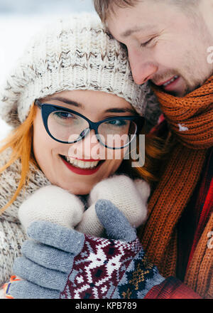 Sensibile esterna inverno ritratto della coppia felice. L'uomo bello è avvolgente e tenendo le mani della sua fidanzata. Close-up. Foto Stock