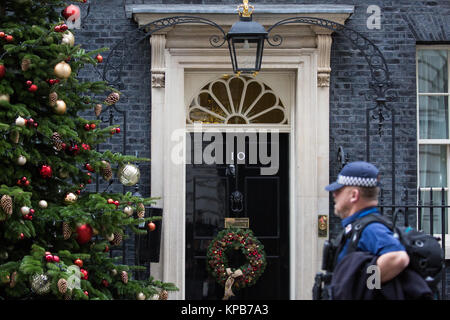 Londra, Regno Unito. 5 dicembre, 2017. Un funzionario di polizia delle Nazioni Unite passa davanti a un albero di Natale e la corona esterna 10 di Downing Street. Foto Stock