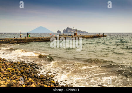 Costa rocciosa imbarco molo dell'isola di Panarea e sullo sfondo il vulcano Stromboli e due scogli emergenti dal Mar Tirreno Foto Stock