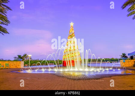 Grand Cayman, Isole Cayman, Dec 2017, albero di Natale in Camana Bay al crepuscolo con una fontana nella parte anteriore di esso Foto Stock