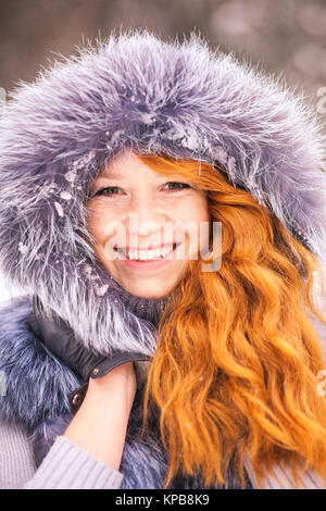 Ritratto di sorridere lo zenzero inverno ragazza cercando allegramente a telecamera. Close up di bellezza viso di giovane donna in pelliccia invernale abbigliamento esterno a snowy co Foto Stock