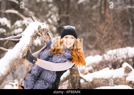 Inverno ragazza bella. Ritratto di piuttosto giovane ragazza vestita di pelliccia in inverno alberi innevate sullo sfondo. La bellezza della donna avente divertimento fuori in legno su Foto Stock