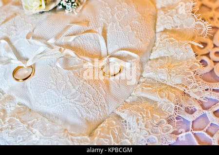 Doppio oro anelli vincolati su un cuscino bianco bianco a forma di cuore Foto Stock