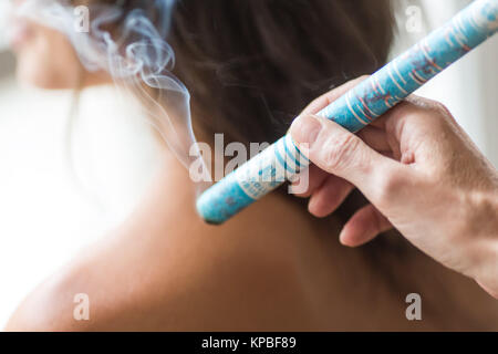 Agopuntore tenendo un covare moxa pole vicino a una spalla del paziente durante un indiretto moxibustione di trattamento. Foto Stock