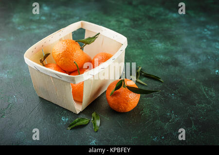 Cesto di mandarini freschi su uno sfondo verde scuro Foto Stock