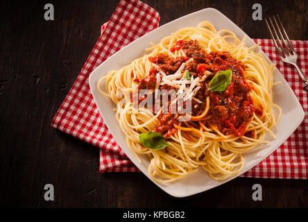 Italiano tradizionale di pasta con salsa bolognese guarnita con formaggio grattugiato e basilico fresco in un ristorante rustico con verifica igienico, elevato angolo vista da sopra al buio su un contatore Foto Stock