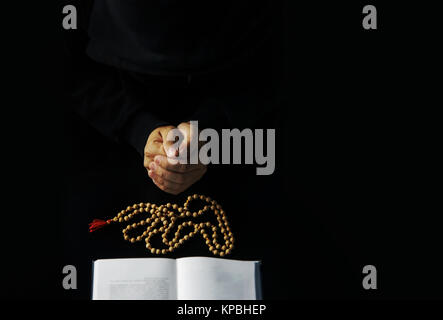 Le mani del giovane sacerdote con la Bibbia e il legno di sandalo il rosario Foto Stock