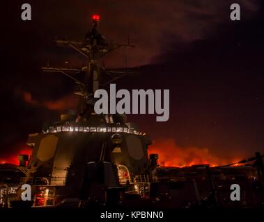 Gli Stati Uniti Navy Arleigh Burke-class guidato-missile destroyer USS Sterett siede pierside presso la base navale di contea di Ventura di notte come Thomas wildfire brucia in background Dicembre 5, 2017 in Port Hueneme, California. Foto Stock