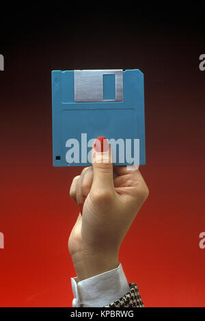 1991 STORICA MANO DI DONNA CHE TIENE BLU 3,5 POLLICI MICRO FLOPPY DISC (©IBM CORP 1973) SU SFONDO ROSSO CHIARO Foto Stock