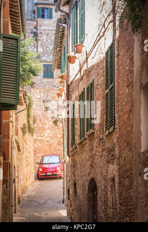 Caratteristica e bella strada laterale in Toscana, con un rosso Fiat 500, Cinquecento parcheggiata in distanza. Foto Stock