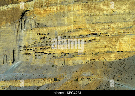 Grotta di antiche abitazioni scavate in un gigantesco rupe sopra Chuksang, Mustang superiore. Minuscolo silhouette di un viaggiatore visibile in basso a destra. Foto Stock