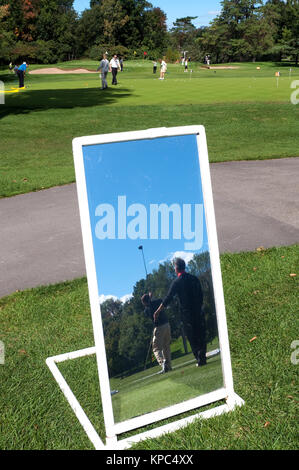 Gli amanti del golf pratica su un driving range, visto in uno specchio utilizzato per le lezioni. Foto Stock