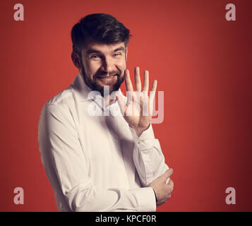 Sorridenti barbuto imprenditore agitando la mano e dire ciao in moda stile bianco shirt su sfondo rosso. Closeup tonica ritratto Foto Stock