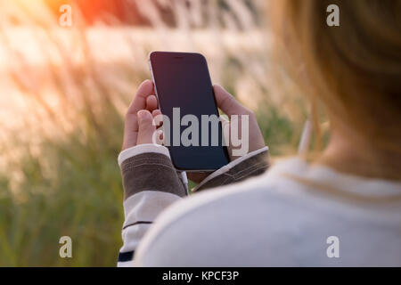 Donna che mantiene smartphone durante il tramonto Foto Stock