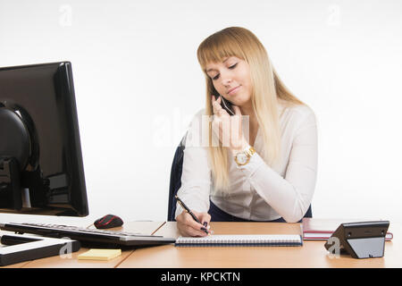 Il segretario iscritto in un notebook informazioni ricevute tramite telefono Foto Stock