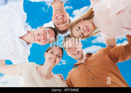 Happy amici formare Huddle contro Sky Foto Stock