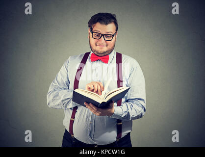 Uomo di contenuto in occhiali lettura interessante libro guardando un po' stupito. Foto Stock