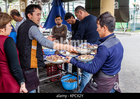 Gli uomini cucinare e servire PLOV (il piatto nazionale) presso l'Asia Centrale del centro di Plov, Tashkent, Uzbekistan Foto Stock