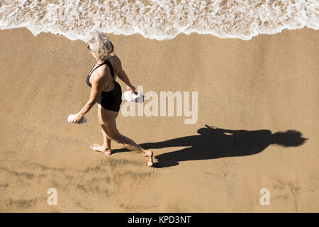 Donna matura in costume da bagno camminando sulla spiaggia in Spagna Foto Stock
